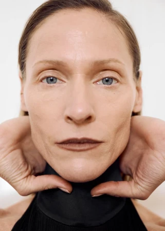 Close-up portrait of model Lindsay Sullivan framing her jawline with her hands against a plain white background.
