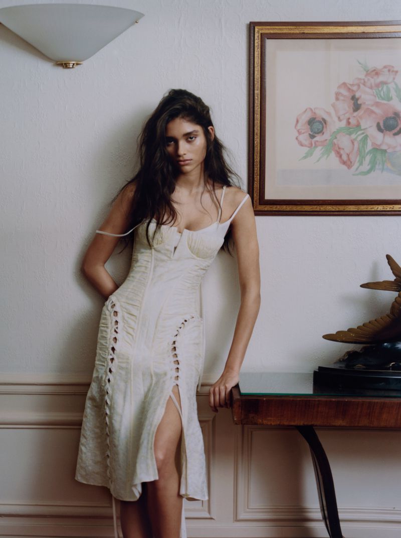 Elegant woman in a white dress posing in an indoor setting, complemented by classic interior decor, natural lighting, and soft color palette.
