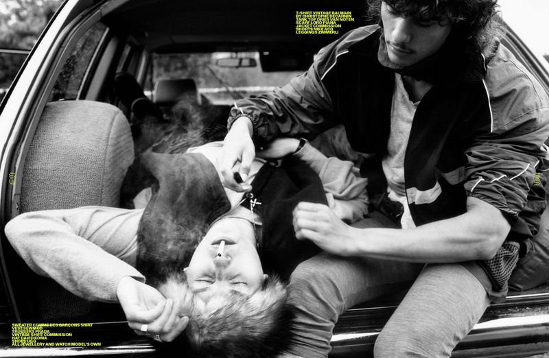 Two adult men in a car interior, one lying down with a cigarette, the other sitting upright. Black and white fashion editorial.