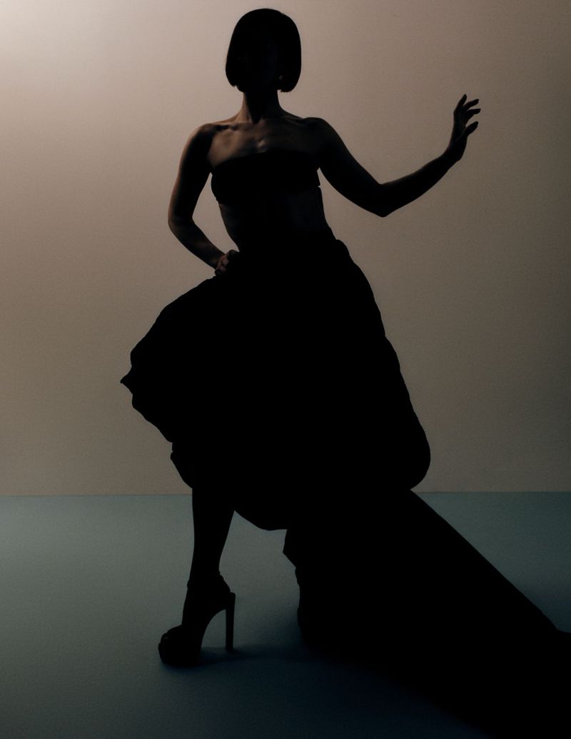 Silhouette of a woman in an elegant dress and high heels posing against a gradient background in a fashion or beauty context.