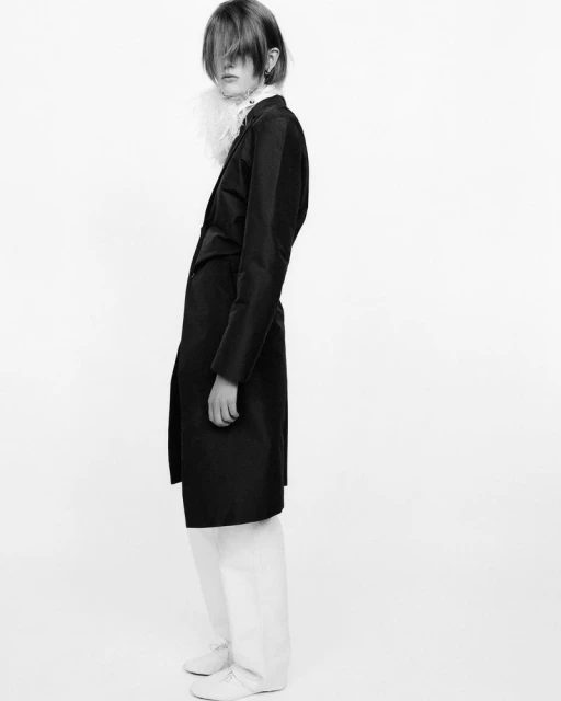 Monochromatic fashion portrait of a female model in a dark coat and white pants against a stark background, showcasing minimalist style.