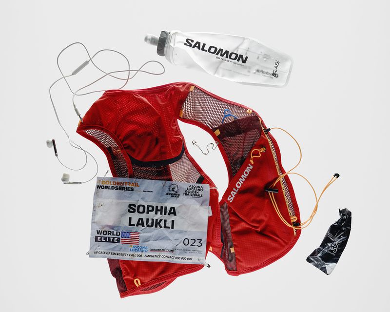 Still life shot of Salomon trail running vest, water bottle, energy gel, and headphones against a white backdrop for Visie search.