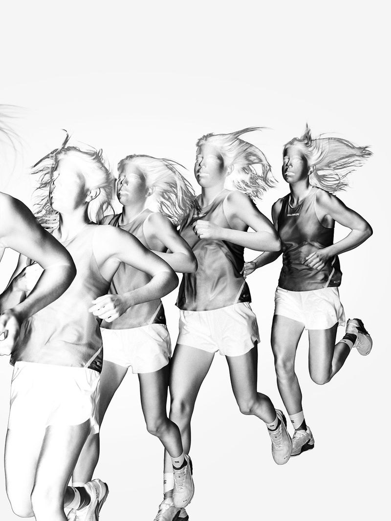 Monochrome image of a female athlete running, captured with a motion blur effect on a white background, showcasing speed and energy.