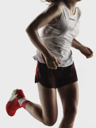 Runner mid-stride wearing a white tank top, dark shorts, and red running shoes against a seamless white background.