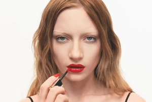 Model Kai Schreiber applying glossy bright red liquid lipstick with a wand against a white background for Haus Labs.