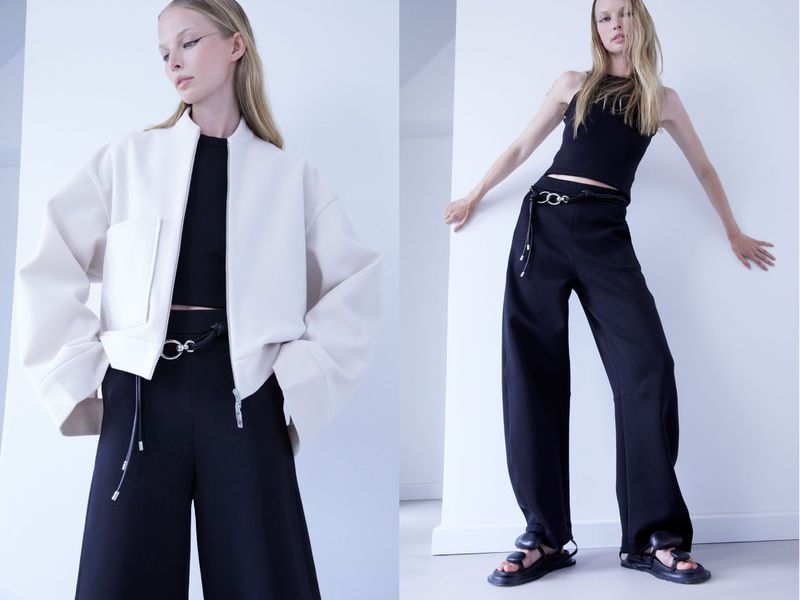 Two fashion models pose in front of a white wall wearing black and white tops with wide-legged black pants and black sandals.
