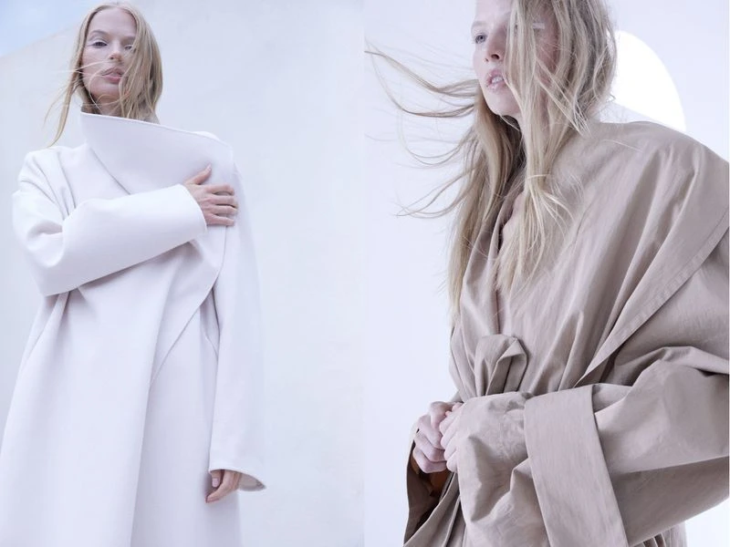 Two fashion models pose in light-colored coats in a studio, with minimalistic aesthetic, creating a modern and clean fashion statement.