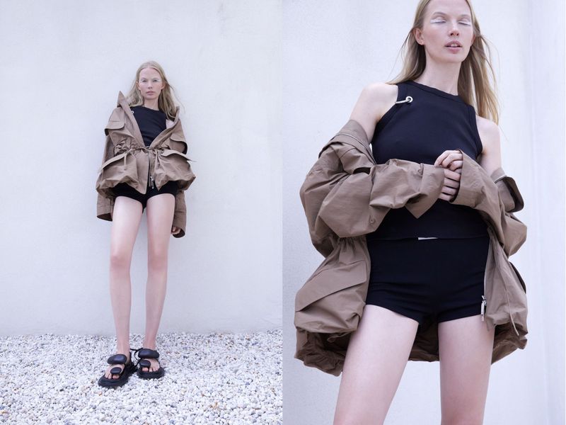 Fashion photo featuring a model in a brown jacket, black top, and shorts, paired with chunky sandals against a plain background.