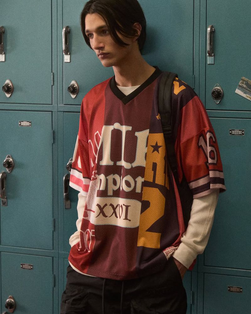 A young adult poses indoors in a jersey with lockers in the background. The lighting is soft and diffused.