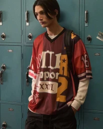 Model Rubuen Bilan-Carroll standing in front of teal metal lockers wearing an oversized graphic jersey shirt.