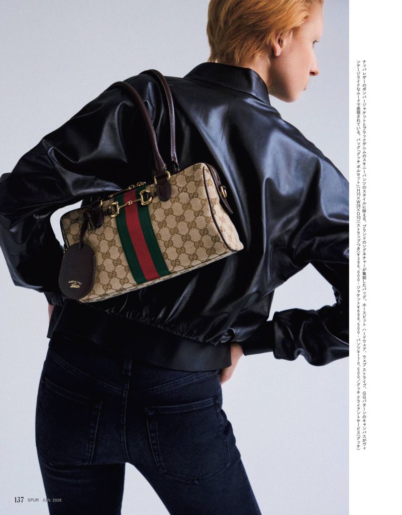 Model with a Gucci handbag wearing a black leather jacket and jeans in a fashion editorial shot against a light background.