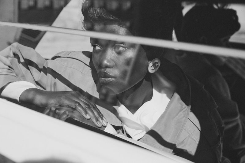 Black and white close-up shot of a woman wearing a button-down shirt and earring, looking off into the distance through a window.
