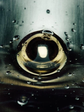 Macro shot of a water droplet with circular refraction effect on a reflective metal surface with smaller water droplets scattered around.