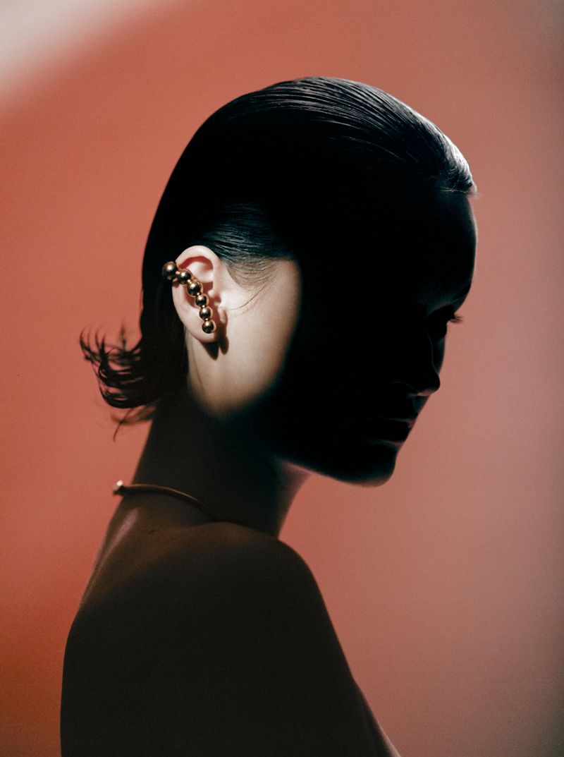 Woman's profile in a photo studio, illuminated by a red gel light highlighting her gold jewelry. Her wet hair is slicked back.