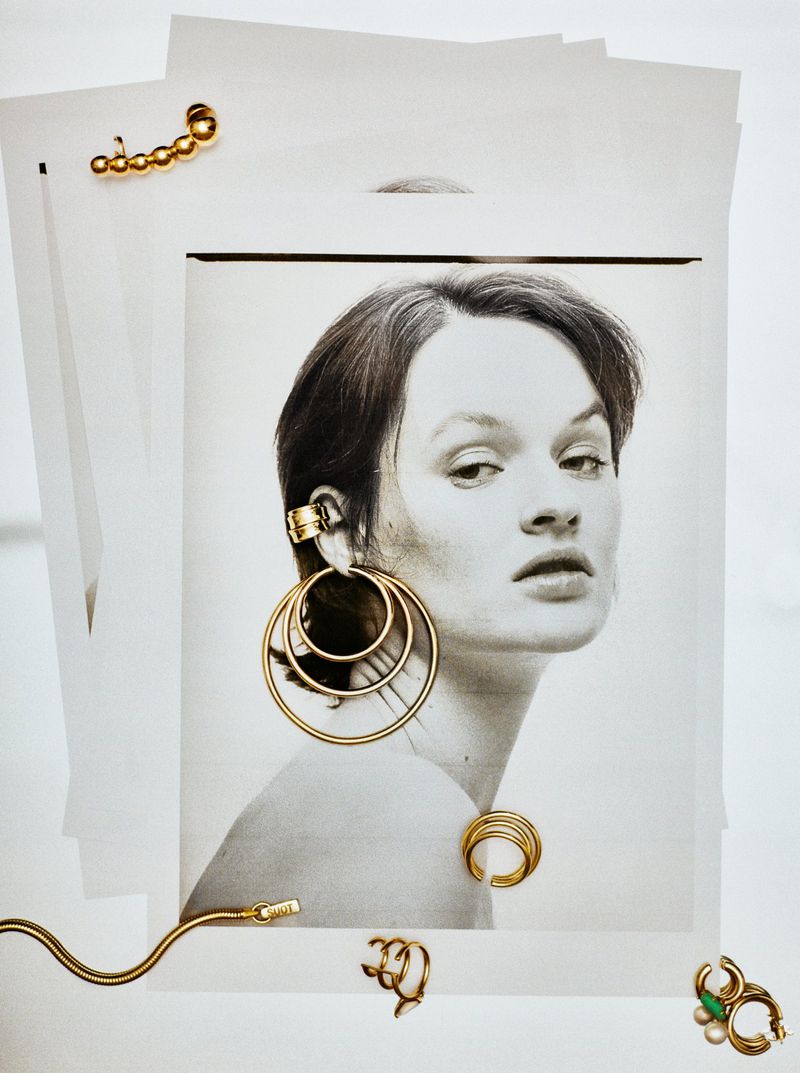 Editorial fashion shot showcasing a black and white portrait of a woman with golden ear cuffs and earrings against a white background.