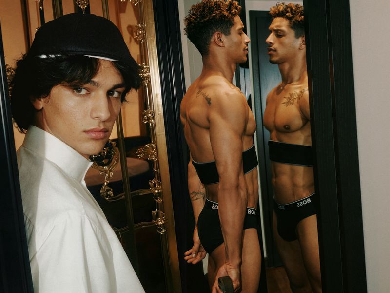 Two male fashion models pose indoors in a close-up shot featuring underwear; one looks directly at the camera, the other to the side.