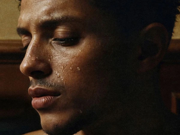 Close-up profile of adult man with sweat droplets on his face, looking down with eyes closed, showing the details of skin and hair.