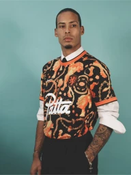 Virgil van Dijk wearing a black and orange Patta graphic jersey over a collared shirt and tie against a teal backdrop.