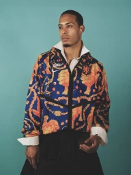 Virgil van Dijk wearing a patterned blue and orange jacket over a white collared shirt against a turquoise background.