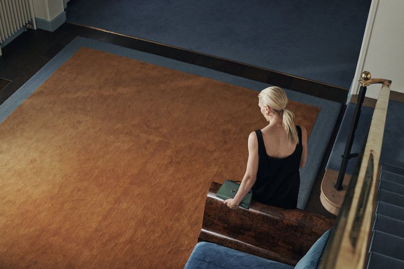 Woman in black dress ascends carpeted stairs with a green purse, captured from a high angle highlighting interior architecture and design.