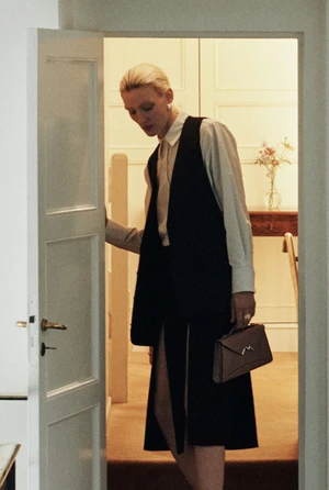 Model Maggie Maurer holding a Moynat handbag while opening a white interior doorway