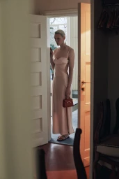 Model Maggie Maurer wearing a silk slip dress holding a handbag in a doorway for Moynat