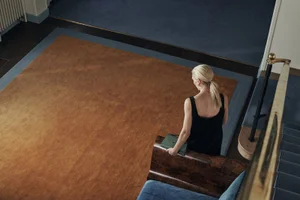 High-angle view of blonde woman in black top holding a green handbag descending stairs in an interior hall