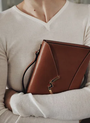 Model wearing a white v-neck ribbed sweater holding a brown leather Moynat handbag with metallic clasp