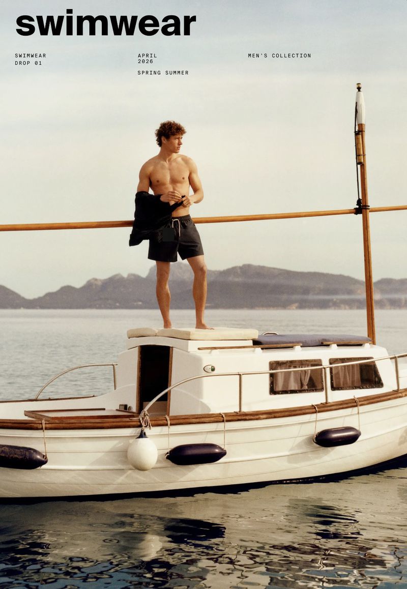 Shirtless man on a white boat with an ocean and island background, advertising swimwear from the Men's Collection for Spring/Summer.