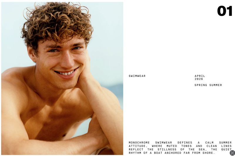 Close-up portrait of a smiling man with curly brown hair in a swimwear advertisement. Set against a blurred outdoor background.