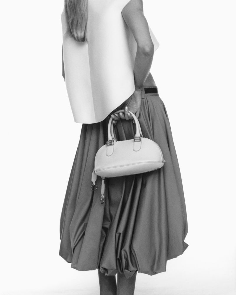 Fashion shot of a woman in a white top and a large skirt, holding a white purse. Black and white studio fashion.