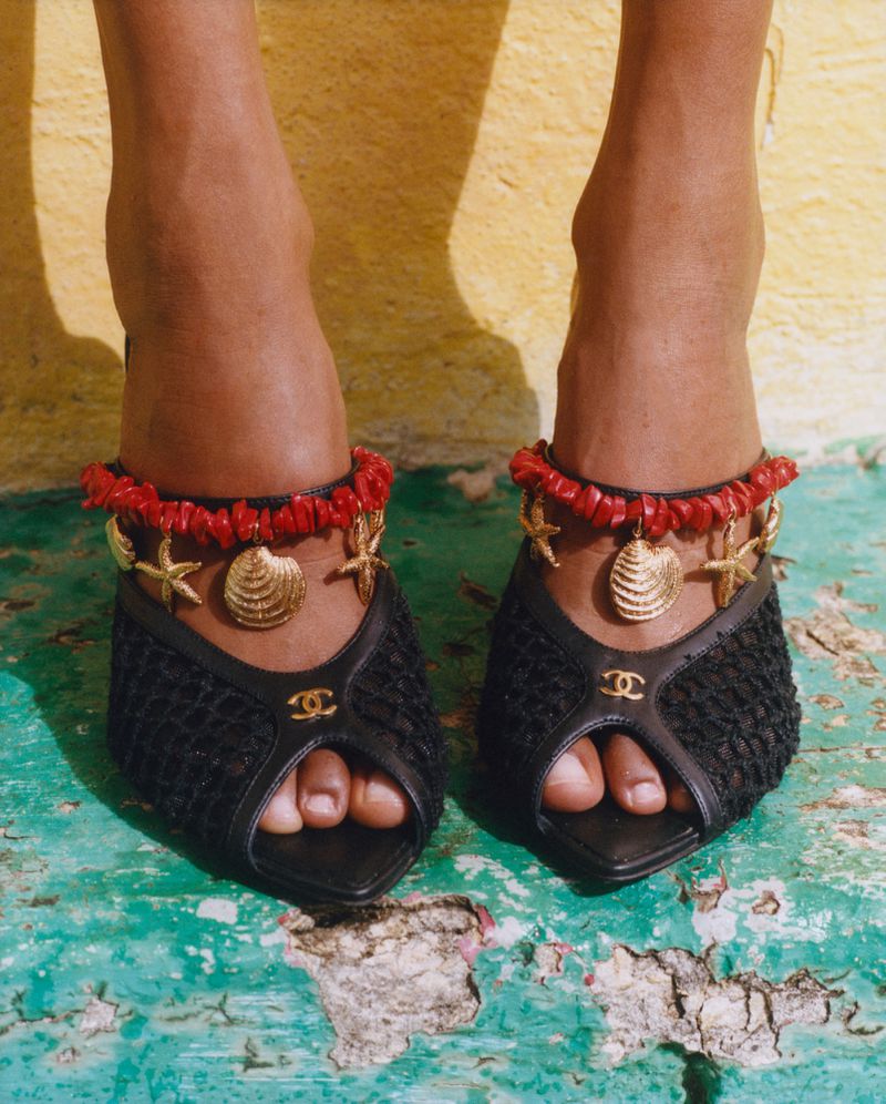 Close-up shot of a person's feet adorned with ankle jewelry and stylish black open-toe heels against a textured backdrop.