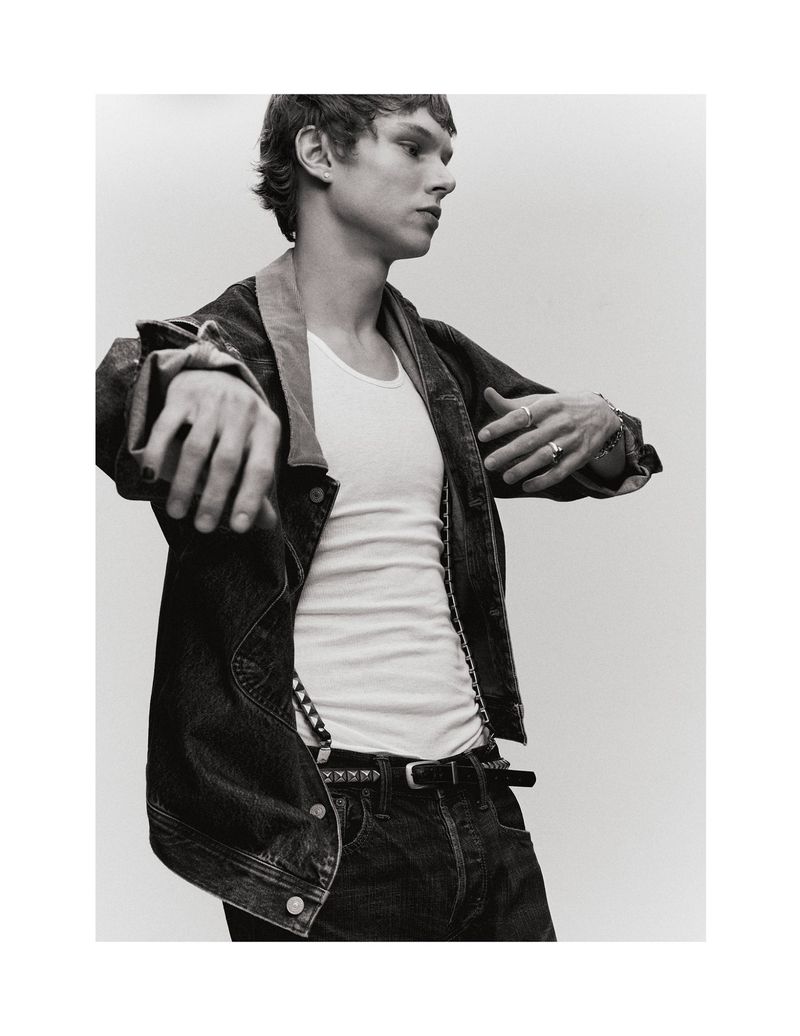 Monochrome portrait of a young adult male in a denim jacket and white t-shirt against a plain background in a studio setting.