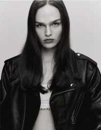 Black and white portrait of a model wearing an open black leather motorcycle jacket over a white band against a studio backdrop.
