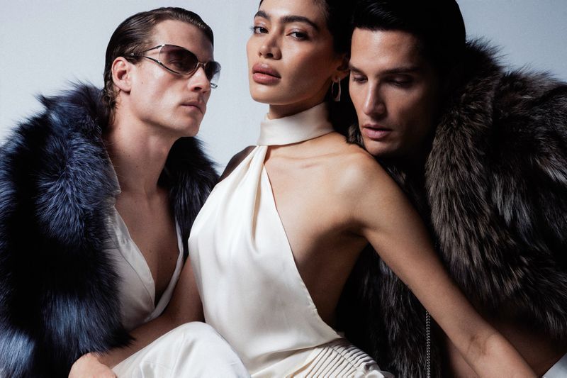Three fashion models pose in a studio setting, wearing elegant clothing and fur coats, showcasing high-end fashion and style.