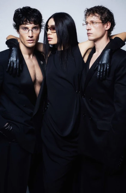 A group shot features three stylish individuals in coordinated black outfits and eyewear, set against a bright, neutral backdrop.