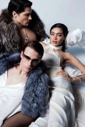 Priscilla Balanta and two male models wearing white satin garments and plush fur stoles posing against a seamless studio backdrop.