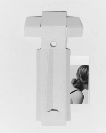 Abstract monochromatic still life featuring a geometric cardboard sculpture and a partial portrait of a woman with a hair bun.