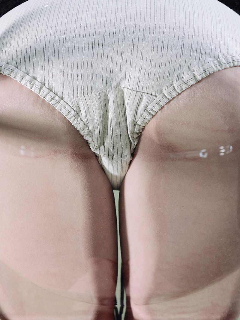 Close-up of a woman in striped swimsuit bottoms standing in water, waist-deep, capturing a minimal and somewhat abstract view.