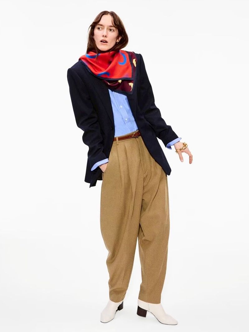 Adult female wearing a navy blazer, scarf, and high-waisted khaki pants, standing in front of a white background in a studio shot.