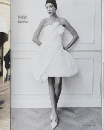 Model wearing a pleated white strapless dress posing against a wall with paneling for Glamour Germany editorial