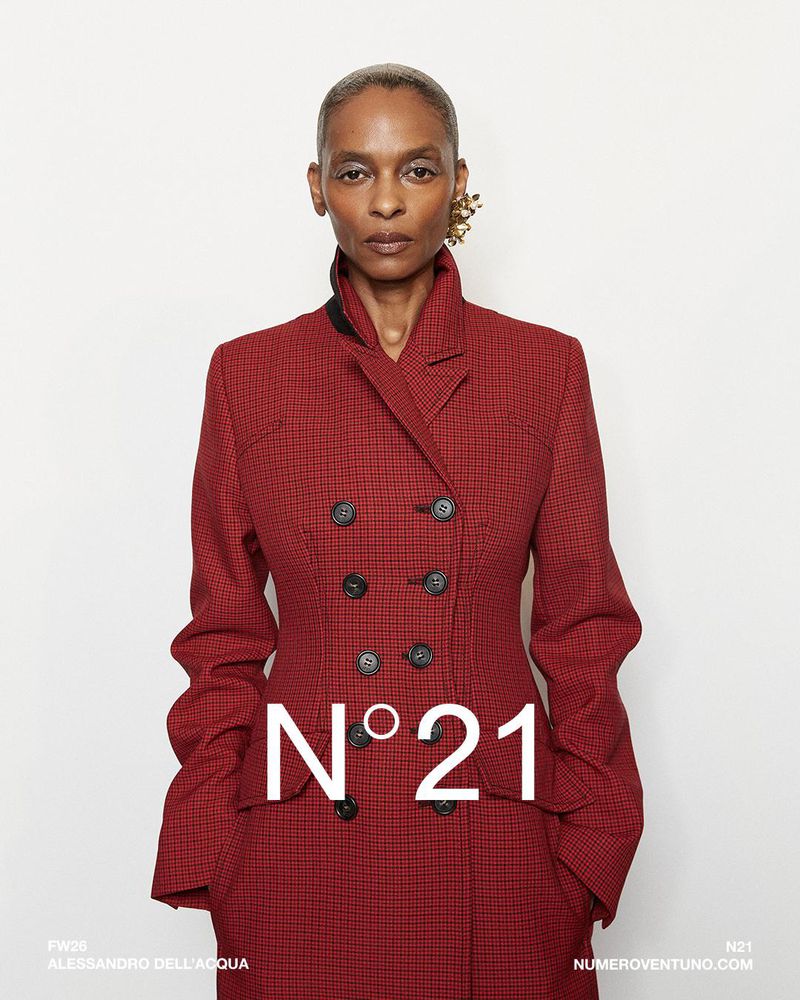 Fashion editorial shot of an adult female wearing a red double-breasted blazer with large gold earrings in a studio setting.