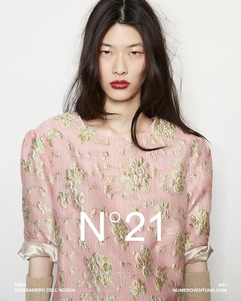 Fashion shot of a female model wearing a pink floral top against a white background. N°21 brand logo overlayed on the dress.