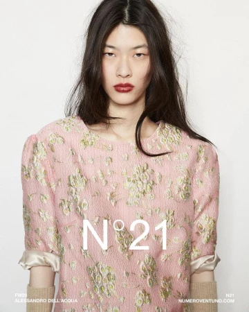 Fashion shot of a female model wearing a pink floral top against a white background. N°21 brand logo overlayed on the dress.