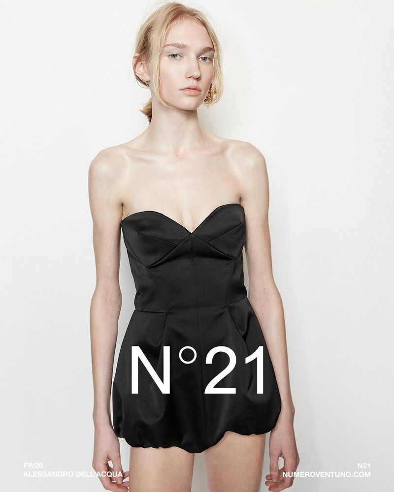 A fair-skinned young woman poses in a black strapless mini-dress against a white backdrop, featuring prominent 'N°21' branding.