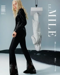 Blonde fashion model in black leather jacket and lace hem trousers standing beside an upside down classical statue on Le Mile cover.