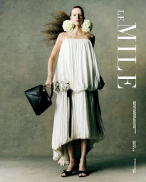 Model Karolina Capkova wearing a pleated white dress and floral earrings while holding a black leather handbag for Le Mile Magazine.