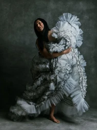 Model Anna Bayle in a voluminous white ruffled dress posing against a dark textured studio background for Vogue Philippines.