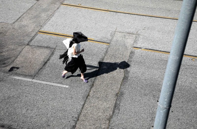 Aerial view of an adult female running on an asphalt road in black and white clothing. Captured from a high angle, providing a blurred context.