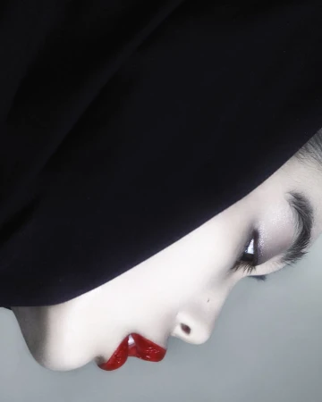 Close-up studio shot of a woman's face in profile, featuring bright red lipstick, dramatic eye makeup, and a black head covering.